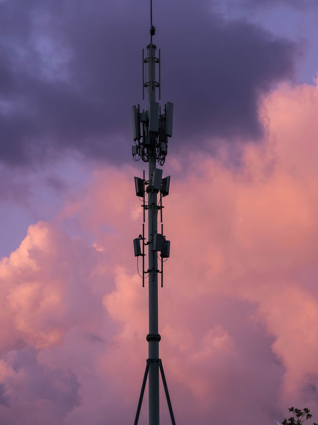 Antena de telecomunicaciones recortada contra un cielo con nubes al atardecer