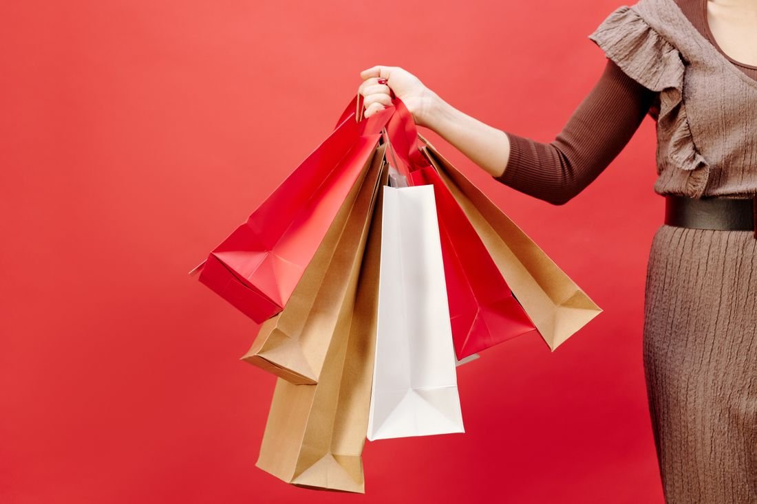 Mujer sosteniendo varias bolsas de compras de papel sobre un fondo rojo