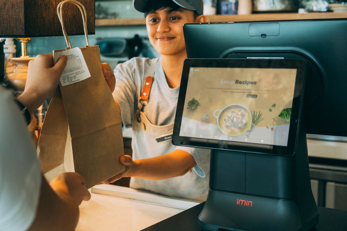 Cajera entregando una bolsa de papel a una clienta en el mostrador de una tienda