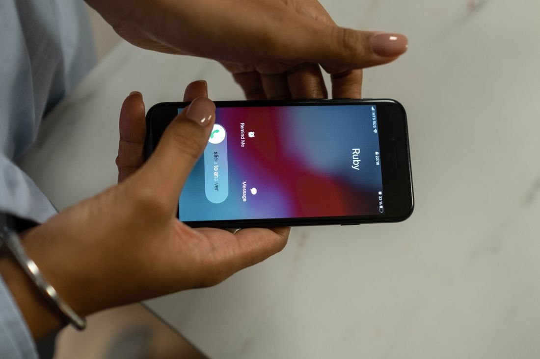 Manos sosteniendo un celular que muestra una llamada entrante sobre una mesa de mármol