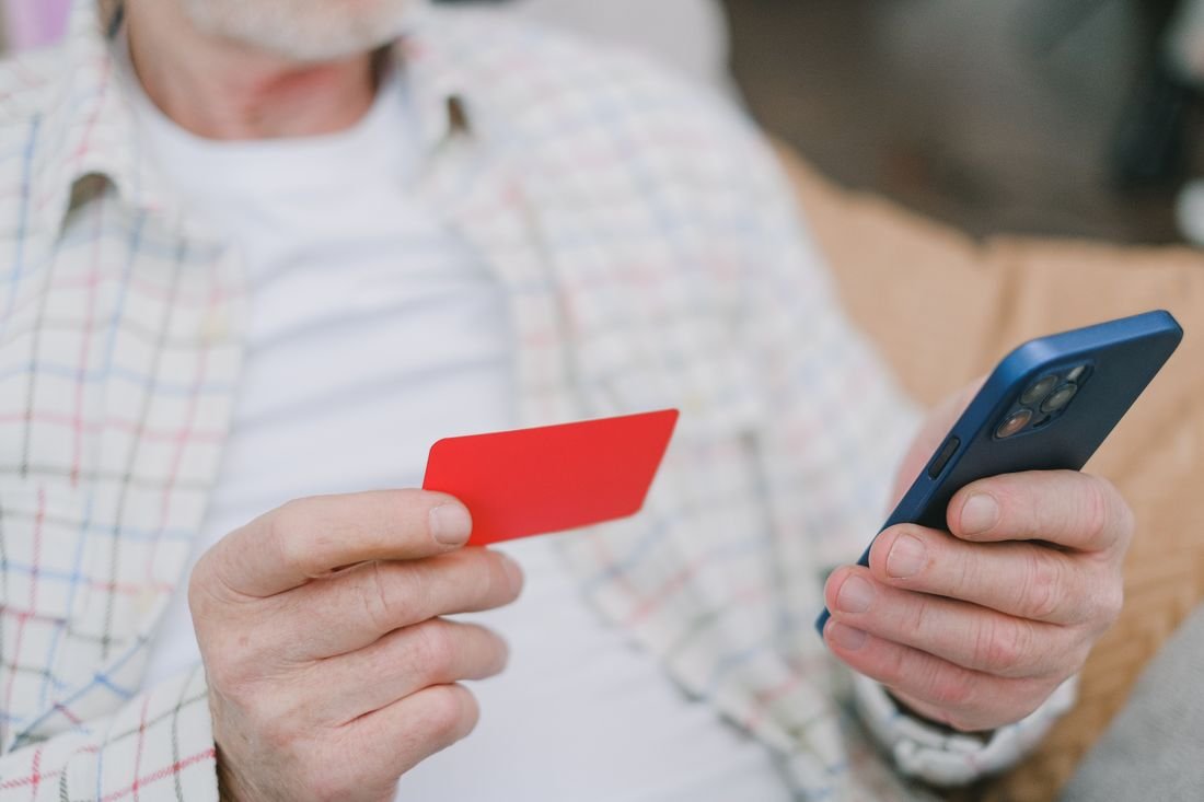 Persona con un celular en una mano y una tarjeta bancaria en la otra a punto de hacer una transferencia