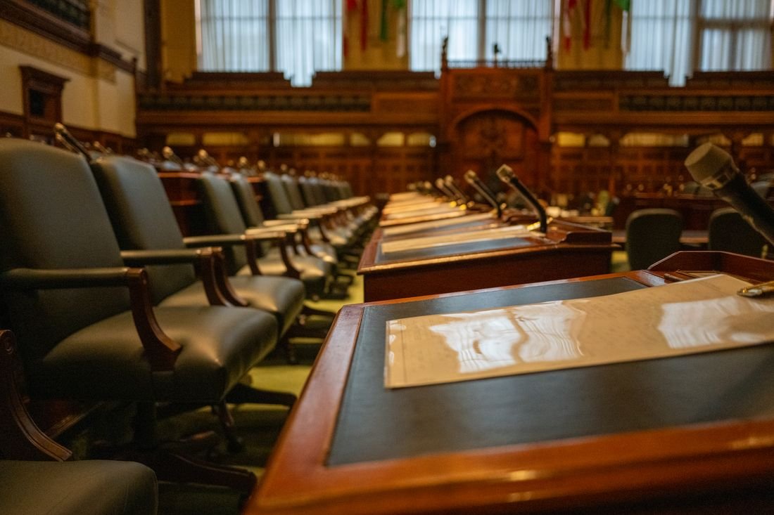 Curules vacías y micrófonos en una sala de sesiones legislativa
