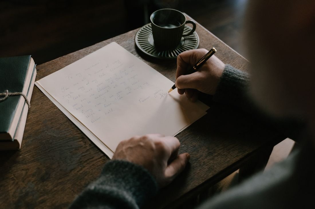 Persona escribiendo una carta a mano sobre una mesa de madera junto a una taza de café