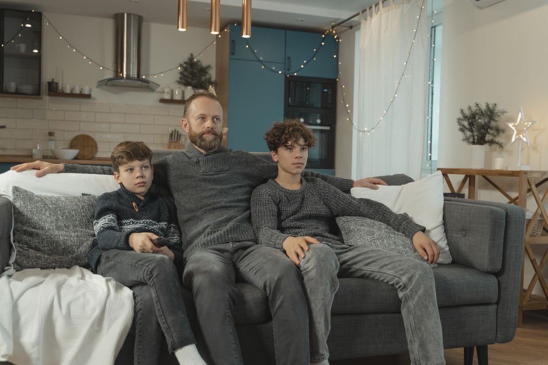 Padre y dos hijos adolescentes viendo televisión sentados en el sofá de la sala