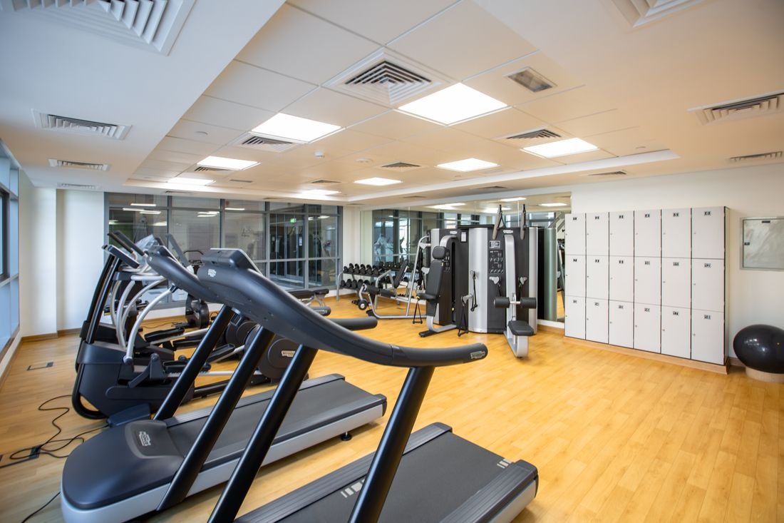 Sala de gimnasio con caminadoras, máquinas de peso y lockers