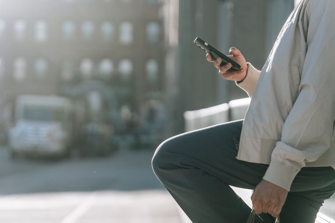 Persona revisando su teléfono móvil en la calle, a contraluz, con la ciudad al fondo