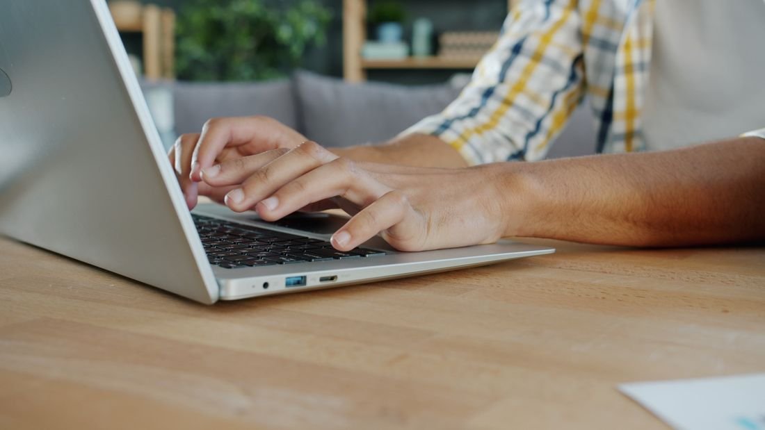 Manos escribiendo en el teclado de un computador portátil sobre una mesa de madera