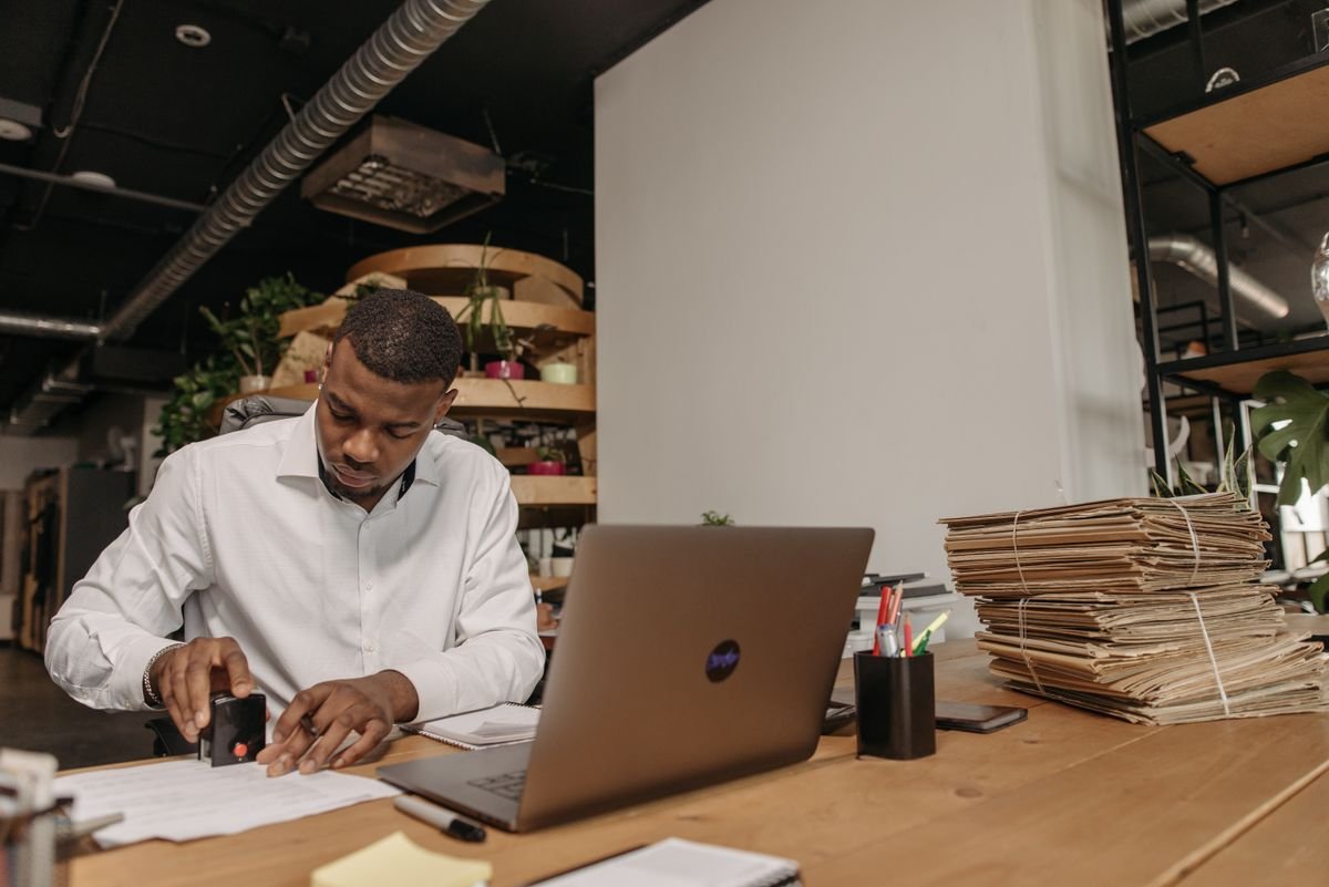 Hombre sellando documentos en el escritorio de una oficina junto a un computador portátil