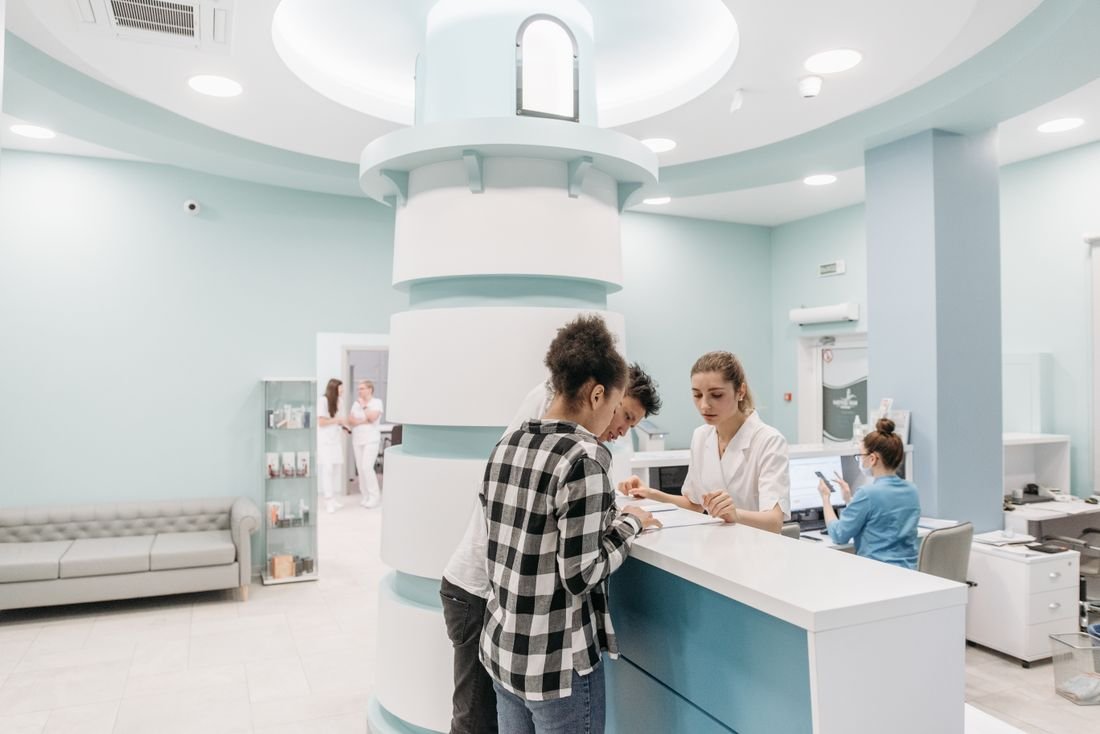 Dos pacientes diligencian un formulario en la recepción de una clínica atendidos por una profesional de la salud