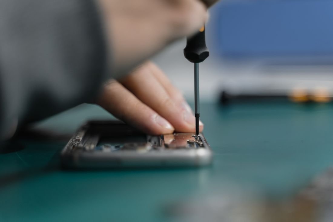 Técnico reparando la placa de un teléfono celular con un destornillador de precisión