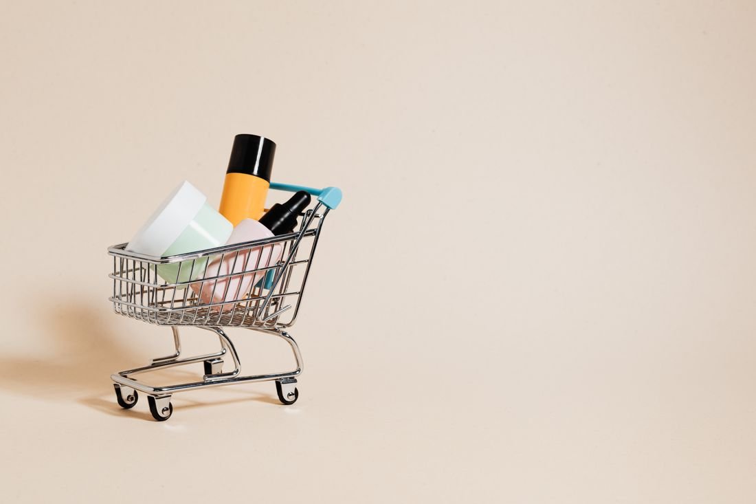 Carrito de compras en miniatura con frascos de cosméticos y cuidado personal sobre un fondo beige
